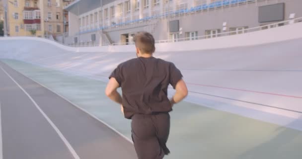 Movimento vista posteriore ritratto di adulto caucasico sportivo corridore maschile jogging sullo stadio nella città urbana all'aperto — Video Stock