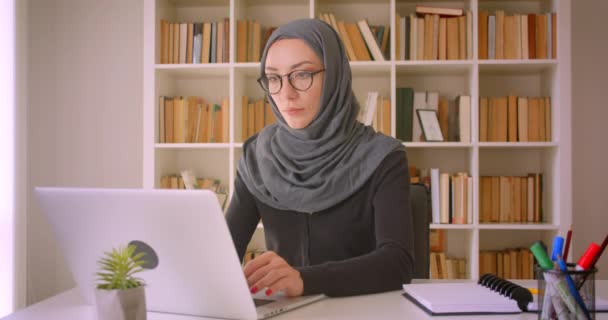 Retrato de close-up de jovem atraente mulher de negócios muçulmana no hijab usando laptop na biblioteca dentro de casa — Vídeo de Stock