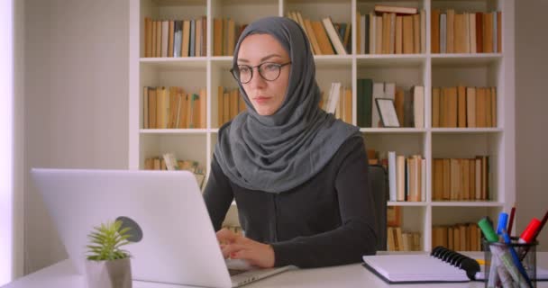 실내 도서관에서 노트북을 사용하여 안경과 히잡을 입은 젊은 매력적인 무슬림 사업가의 클로즈업 초상화 — 비디오