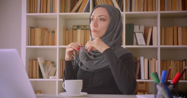 Крупный план портрета молодой привлекательной мусульманки-предпринимательницы в хиджабе с помощью ноутбука, заботливой и пьющей кофе в библиотеке в помещении — стоковое видео