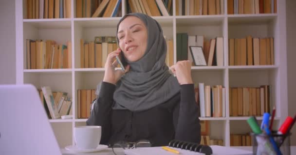 Gros plan portrait de jeune femme d'affaires musulmane attrayante dans le hijab ayant un appel téléphonique assis devant un ordinateur portable dans la bibliothèque à l'intérieur — Video