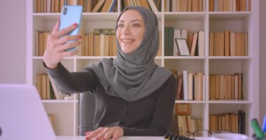 Hijab genç çekici Müslüman iş kadını closeup portre kapalı kütüphanede dizüstü bilgisayar önünde oturan telefonda bir görüntülü görüşme olan