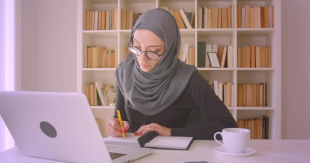 히잡에서 젊은 매력적인 무슬림 사업가의 클로즈업 초상화 는 실내 도서관에서 메모를 복용 노트북에 화상 통화를 갖는 — 비디오