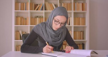 Gözlük ve hijab kütüphane kapalı notlar alan genç çekici Müslüman iş kadını Closeup portre