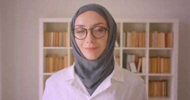 Gözlük ve başörtüsü genç müslüman kadın doktor kapalı kütüphanede mutlu bir şekilde gülümseyen kameraya bakarak Closeup portre