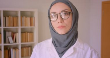 Gözlük ve başörtüsü genç Arap kadın doktor kapalı kütüphanede neşeyle gülümseyen kameraya bakarak Closeup portre
