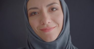 Türbanlı genç çekici müslüman kadının, gri zemini izole edilmiş arka planla neşeyle gülümseyen kameraya bakan yakın çekim portresi
