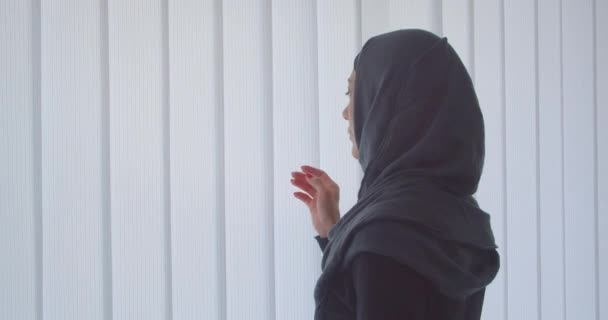 Primo piano ritratto di giovane donna musulmana attraente in hijab guardando attraverso la finestra con tulle all'interno in appartamento — Video Stock