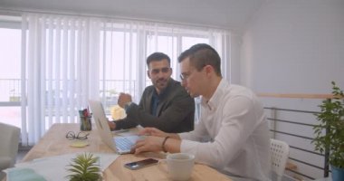 Dizüstü bilgisayarı kullanan ve kapalı ofiste tartışma olan iki yetişkin kafkasyalı başarılı işadamının portresi