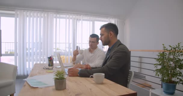 Portret van twee volwassen Kaukasische zakenlieden met behulp van de laptop en het hebben van een gesprek — Stockvideo