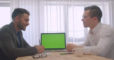 Ofis kapalı işyerinde yeşil renk anahtar ekranı ile dizüstü bilgisayar ile resmi bir tartışma iki yetişkin başarılı işadamlarının Portresi