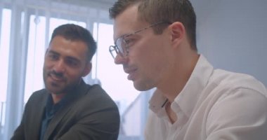 İki neşeli kafkas işadamının kapalı mekanda birlikte çalışan yakın çekim portresi. Bir dizüstü bilgisayarda yazma başka notlar alarak