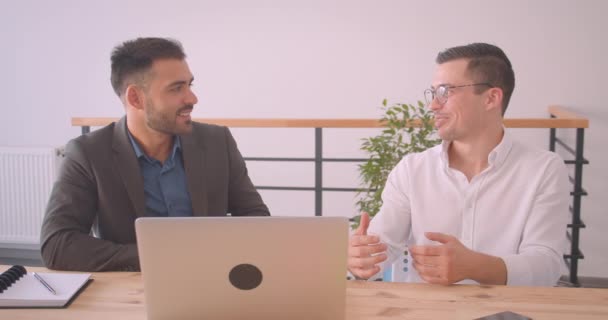 Κοντινό πορτρέτο δύο επιτυχημένων Καυκάσιων επιχειρηματιών που συζητούν ένα έργο για το φορητό υπολογιστή μαζί στο γραφείο σε εσωτερικούς χώρους — Αρχείο Βίντεο
