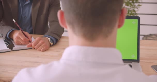 Close-up portret van twee aantrekkelijke zakenlieden met behulp van de laptop met groene Chroma scherm in het kantoor binnenshuis — Stockvideo