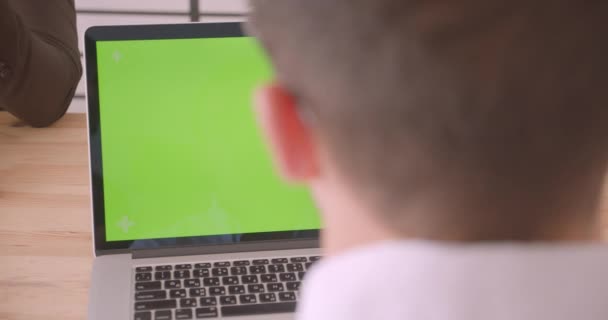 Nahaufnahme Rückseite Porträt des kaukasischen Geschäftsmannes mit dem Laptop mit grünem Chroma-Schlüsselbildschirm im Büro drinnen — Stockvideo