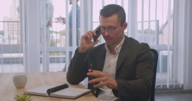 Gözlüklü çekici işadamının işyerinde kapalı ofiste telefon görüşmesi yaptığı closeup portresi