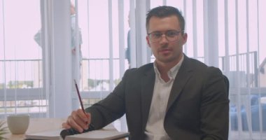 Gözlüklü çekici işadamının kapalı ofiste mutlu bir şekilde gülümseyen kameraya bakan yakın çekim portresi