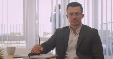 Gözlüklü çekici işadamının kapalı ofiste neşeyle gülümseyen kameraya bakan yakın çekim portresi