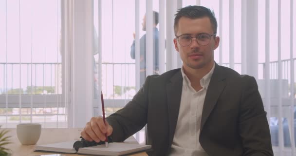 Retrato de close-up de empresário atraente em óculos olhando para a câmera sorrindo alegremente no escritório dentro de casa — Vídeo de Stock