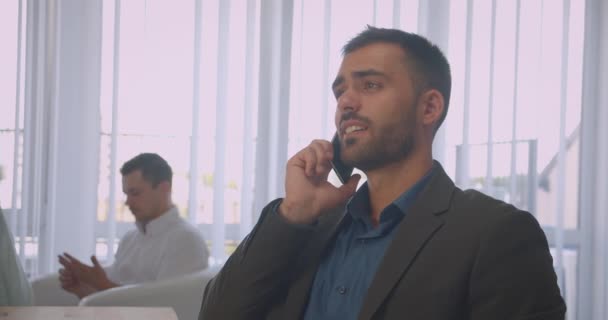 Крупный план портрета привлекательного бизнесмена, счастливо разговаривающего по телефону в офисе в помещении на рабочем месте — стоковое видео