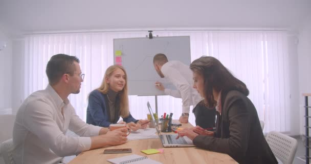 4人の同僚の肖像画が集まり、屋内で職場で話し合う。ホワイトボードにグラフを描くビジネスマン — ストック動画