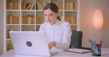 Genç çekici kafkas iş kadınının dizüstü bilgisayarı kullanarak kapalı ofiste mutlu bir şekilde gülümseyen kameraya bakan yakın çekim portresi