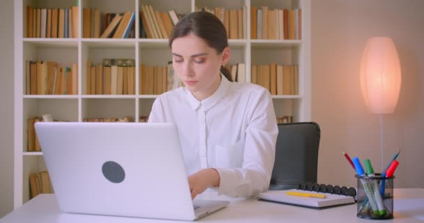 Nahaufnahme Porträt einer jungen attraktiven kaukasischen Geschäftsfrau mit dem Laptop, die im Büro drinnen in die Kamera schaut — Stockvideo