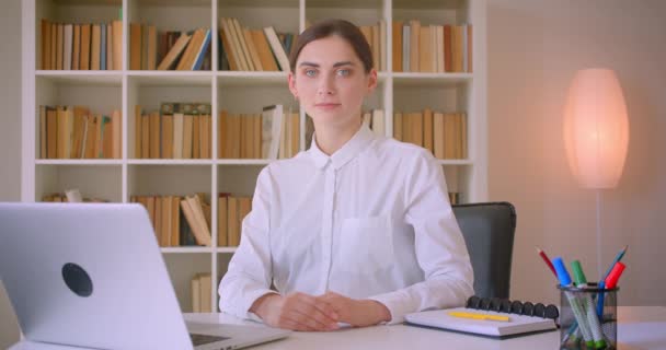Närbild porträtt av unga attraktiva kaukasiska affärskvinna tittar på kamera leende glatt sitter framför den bärbara datorn på kontoret inomhus — Stockvideo