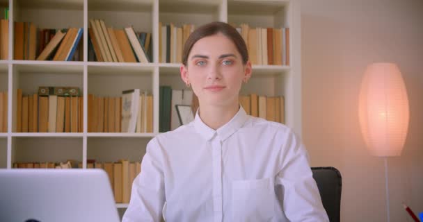 Retrato de cerca de la joven mujer de negocios caucásica mirando a la cámara sonriendo alegremente sentada frente al portátil en la oficina en el interior — Vídeos de Stock