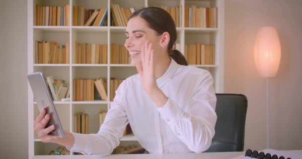 Närbild porträtt av unga kaukasiska affärskvinna med ett videosamtal på tabletten vinka Hej och pratar glatt på kontoret — Stockvideo
