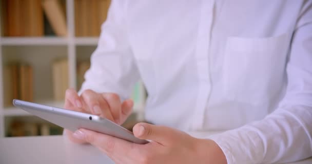 Closeup portrait of young attractive caucasian businesswomans hands typing on the tablet in the office with bookshelves on the background — Stock Video