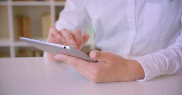 Primer plano retrato de jóvenes atractivas mujeres de negocios caucásicas manos utilizando la tableta en la oficina con estanterías en el fondo — Vídeo de stock