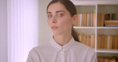 Genç kafkas iş kadını dönüm ve arka planda kitapraflar ile ofiste duran kamera bakarak Closeup portre