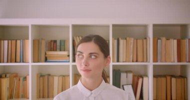 Genç komik kafkas iş kadını arka planda kitaplıklar ile ofiste duran kamera bakarak Closeup portre