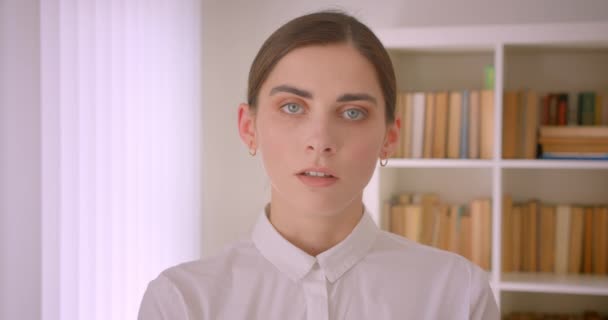 Close-up portret van jonge succesvolle Kaukasische zakenvrouw kijken naar camera staande in kantoor met boekenkasten op achtergrond — Stockvideo
