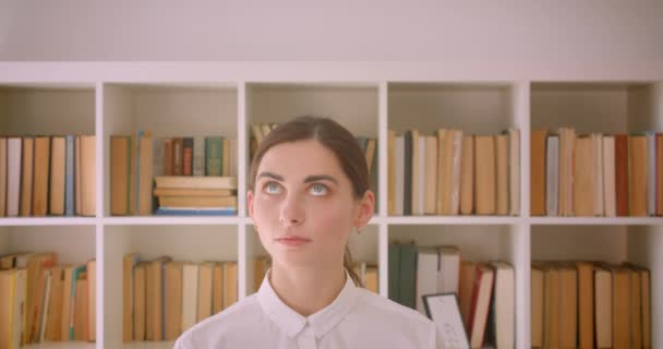 Gros plan portrait de jeune femme d'affaires caucasienne drôle regardant la caméra souriant debout dans le bureau avec des étagères sur fond — Video