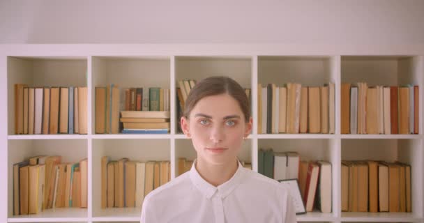 Närbild porträtt av unga roliga kaukasiska affärskvinna tittar på kamera leende lyckligt stående i kontor med bokhyllor på bakgrunden — Stockvideo
