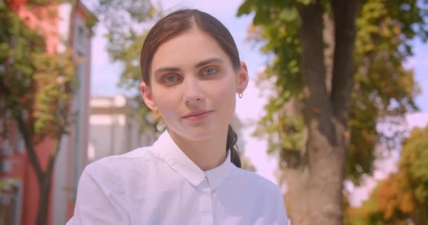 Primer plano retrato de joven atractiva mujer caucásica mirando a la cámara descansando felizmente en el parque al aire libre — Vídeo de stock