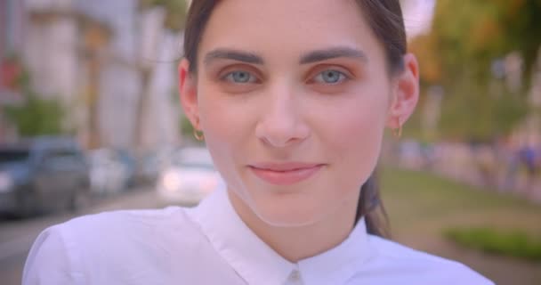 Крупный план портрета молодой красивой кавказской женщины, смотрящей в камеру и радостно улыбающейся, отдыхающей в парке на открытом воздухе — стоковое видео