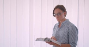 Ofiste evde mutlu bir şekilde gülümseyen bir kitap okuyan gözlüklü genç yakışıklı beyaz işadamının yakın çekim portresi