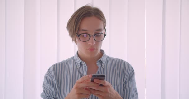 Κοντινό πλάνο του νεαρού όμορφος Καυκάσιος επιχειρηματίας χρησιμοποιώντας το τηλέφωνο στέκεται μέσα στο γραφείο — Αρχείο Βίντεο
