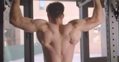 Yakın çekim arka görünüm portre erkeksi gömleksiz kaslı adam spor salonunda kapalı barlar üzerinde çekerek