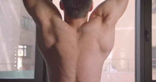 Closeup back view portrait of adult shirtless caucasian man pulling up on bars in the gym indoors — Stock Video