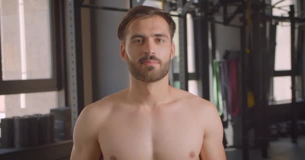 Primer plano retrato de hombre caucásico musculoso sin camisa mirando a la cámara con motivación de pie en el gimnasio en el interior — Vídeos de Stock