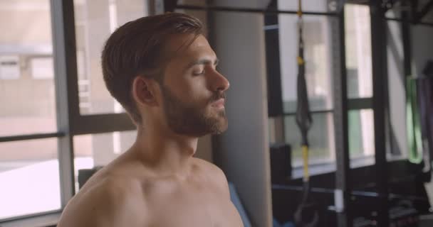 Primer plano retrato de hombre caucásico atractivo sin camisa mirando a la cámara con motivación de pie en el gimnasio en el interior — Vídeos de Stock