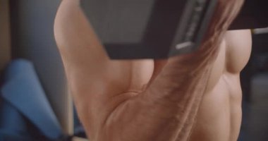 Gömleksiz yakışıklı beyaz adamın kapalı salonda spor salonunda durarak çaba ile dambıllarla çalışan closeup portresi