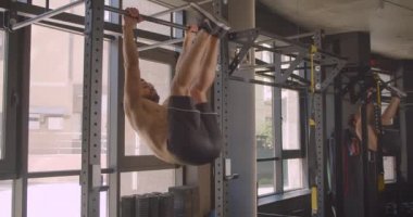 Gömleksiz kaslı beyaz adamın kapalı salonda spor salonunda motive olan barlar üzerinde bacak yükseltir yapıyor Closeup portre