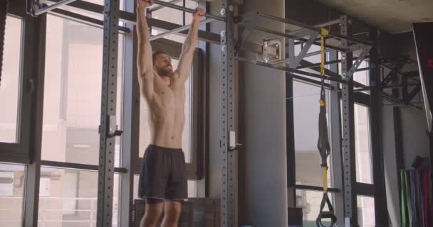 Nahaufnahme Porträt eines hemdlosen muskulösen attraktiven kaukasischen Mannes beim Beinheben am Barren, motiviert in der Halle — Stockvideo
