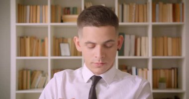 Genç kendine güvenen çekici işadamının arka planda kitaplıklar ile kapalı kütüphane kamera bakarak Closeup portre