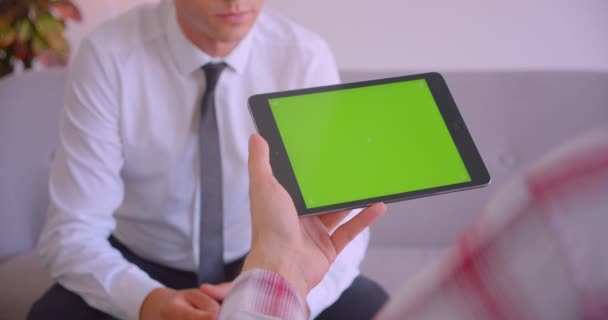 Portrait rapproché du gestionnaire du service à la clientèle parlant à un client tenant une tablette avec écran vert au bureau — Video